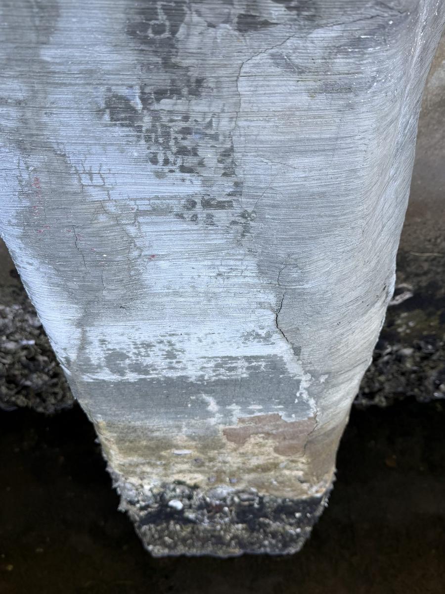 Vertical hairline crack running top to bottom on a concrete seawall cap, widening at the cap edge
